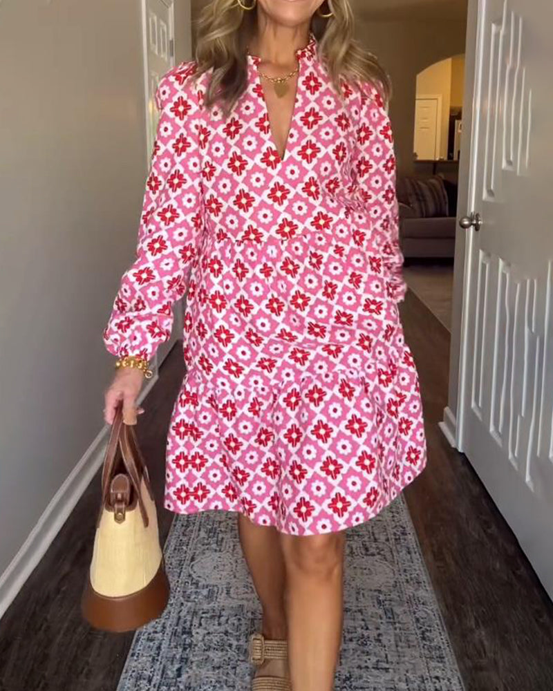 Pink - A woman wearing a pink and red geometric floral print cotton poplin tiered dress with long bishop sleeves and a ruffle neckline, paired with a straw handbag.