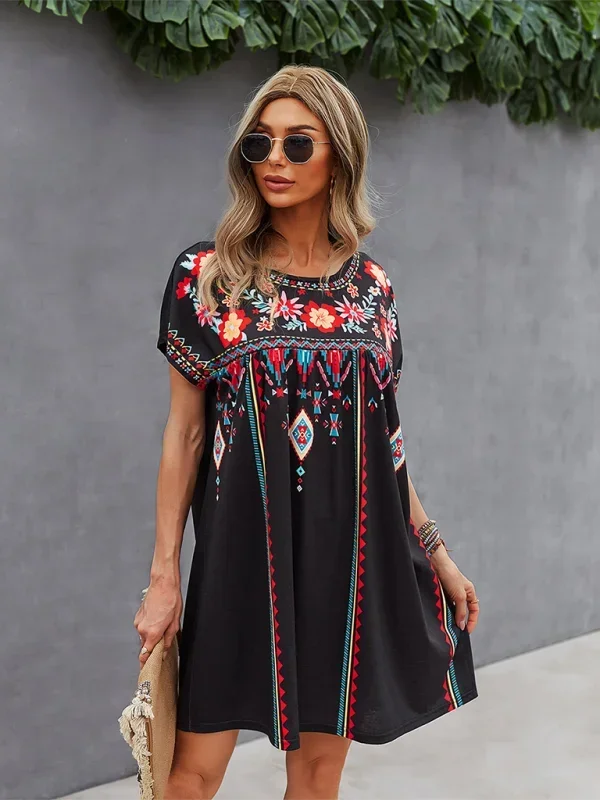 Black short-sleeve mini dress featuring vibrant geometric and floral folkloric patterns with a gathered yoke and relaxed shift silhouette.