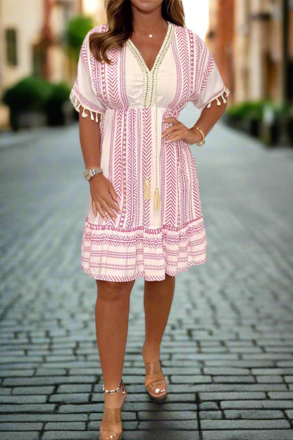 White/Pink - A woman wearing a white short-sleeved mini dress with a black geometric chevron print, featuring a V-neckline with embroidered trim, tassel-detailed flutter sleeves, and an adjustable drawstring waist.