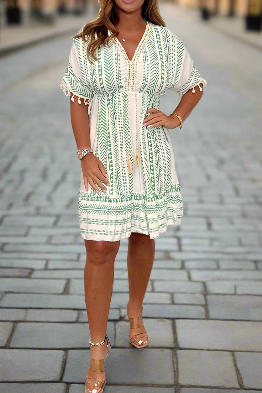 White/Green - A woman wearing a white short-sleeved mini dress with a black geometric chevron print, featuring a V-neckline with embroidered trim, tassel-detailed flutter sleeves, and an adjustable drawstring waist.
