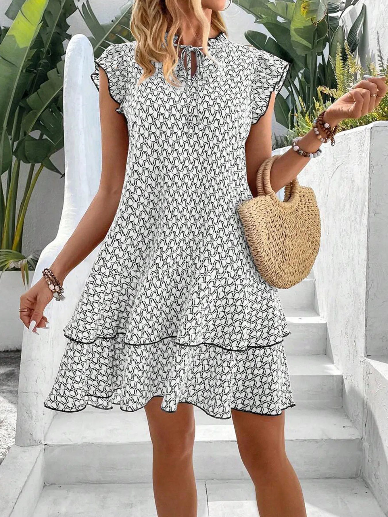Red - A woman wearing a cream and black geometric print mini dress with flutter cap sleeves, a split neckline, and a tiered ruffle hem with dark contrast piping.