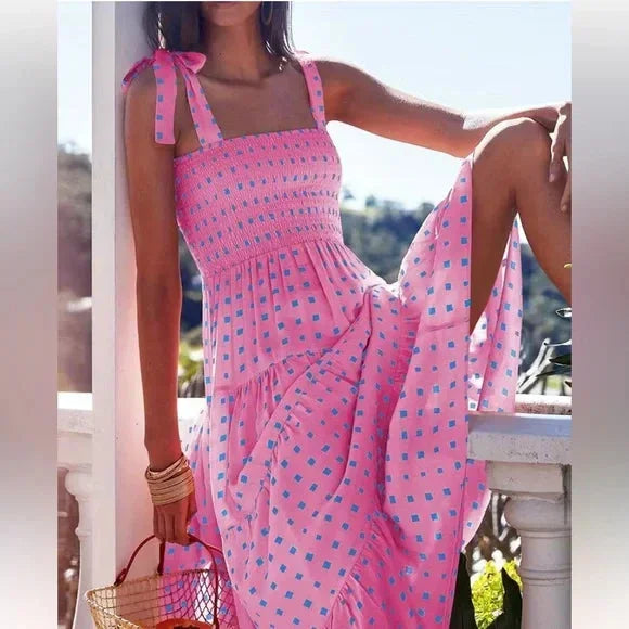 Pink and blue geometric patterned maxi dress featuring a smocked bodice, adjustable tie shoulder straps, and a flowing tiered skirt.