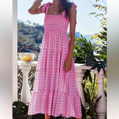 Pink and blue geometric patterned maxi dress featuring a smocked bodice, adjustable tie shoulder straps, and a flowing tiered skirt.
