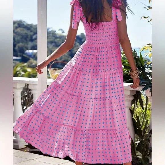 Pink and blue geometric patterned maxi dress featuring a smocked bodice, adjustable tie shoulder straps, and a flowing tiered skirt.
