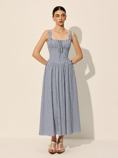 Blue - A woman wearing a blue and white gingham midi dress featuring a square neckline, corset-style bodice with a front tie, and a gathered A-line skirt.