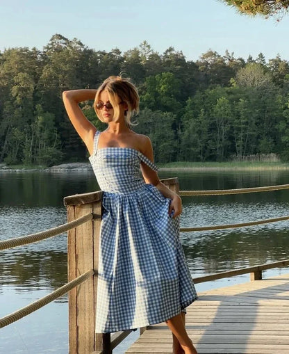 Hue - Woman wearing a blue and white gingham midi dress with a structured corset bodice and full pleated skirt, standing on a wooden dock.