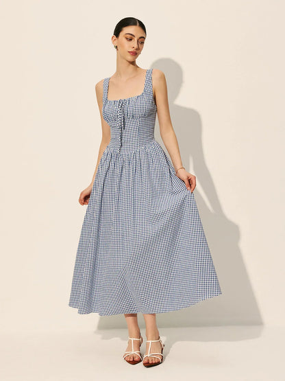 Blue - A woman wearing a blue and white gingham midi dress featuring a square neckline, corset-style bodice with a front tie, and a gathered A-line skirt.