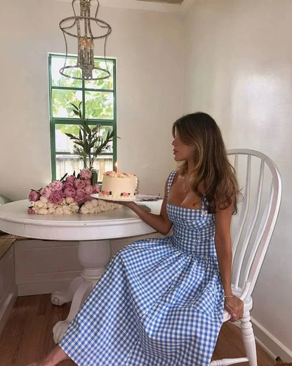 Hue - Woman wearing a blue and white gingham midi dress with a structured corset bodice and full pleated skirt, standing on a wooden dock.
