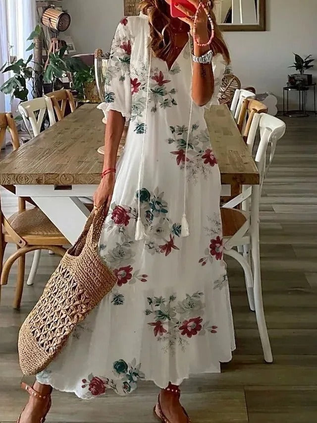 Flowers - A woman wearing a blue and white ikat print maxi dress with a V-neckline, tassel ties, and short sleeves, holding a woven straw tote bag.