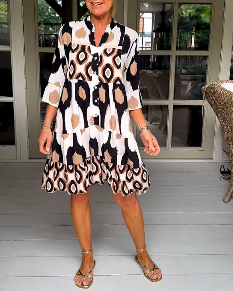 White - A woman wearing a knee-length, tiered tunic dress with a black, tan, and white geometric ikat print, featuring elbow-length sleeves with ruffled cuffs and a split V-neckline.