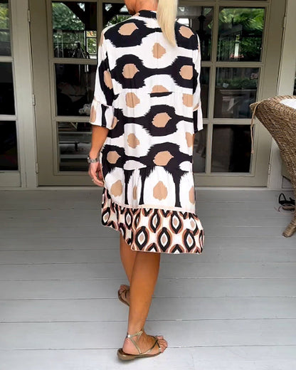 White - A woman wearing a knee-length, tiered tunic dress with a black, tan, and white geometric ikat print, featuring elbow-length sleeves with ruffled cuffs and a split V-neckline.