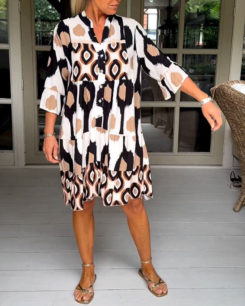 White - A woman wearing a knee-length, tiered tunic dress with a black, tan, and white geometric ikat print, featuring elbow-length sleeves with ruffled cuffs and a split V-neckline.