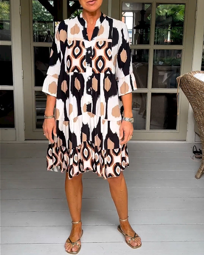 White - A woman wearing a knee-length, tiered tunic dress with a black, tan, and white geometric ikat print, featuring elbow-length sleeves with ruffled cuffs and a split V-neckline.