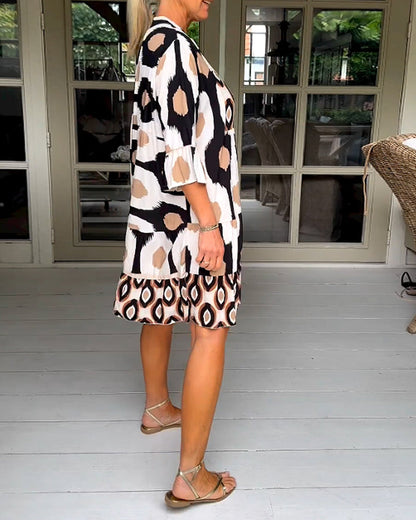 White - A woman wearing a knee-length, tiered tunic dress with a black, tan, and white geometric ikat print, featuring elbow-length sleeves with ruffled cuffs and a split V-neckline.