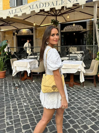 White - Woman wearing a white jacquard mini dress with puff sleeves and a bubble hem, standing on a cobblestone street in front of a restaurant.
