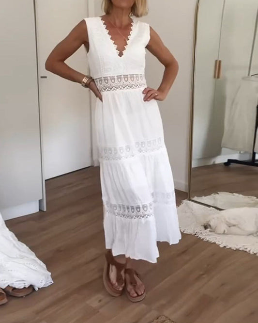 A woman wearing a sleeveless white tiered maxi dress with crochet lace inserts at the waist and skirt, featuring a scalloped V-neckline.