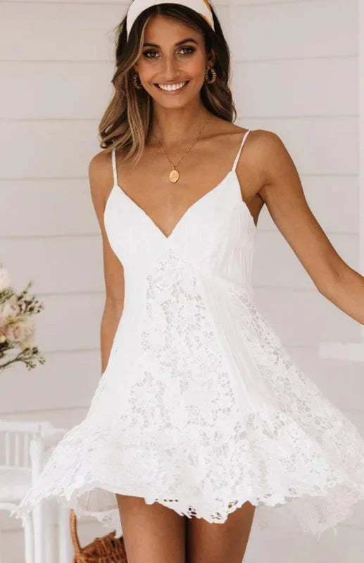 Woman wearing a white V-neck mini dress featuring delicate spaghetti straps and a flared skirt with intricate lace paneling.
