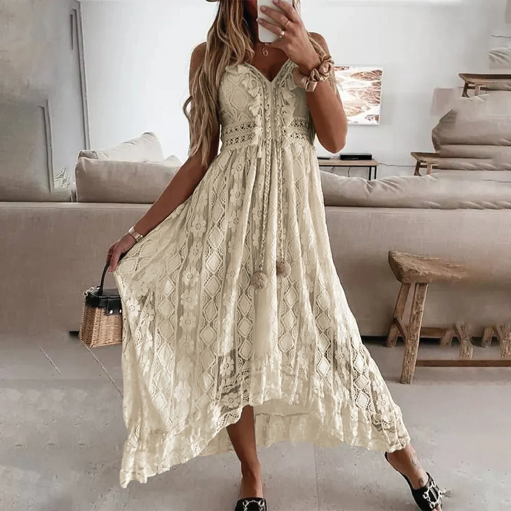 Cream - A woman wearing a white sleeveless high-low maxi dress made of paneled floral lace, featuring a V-neckline, braided tassel ties at the waist, and a flowing hemline.