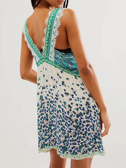 Mint - A woman wearing a sage green bohemian mini slip dress featuring a mixed ditsy floral and rust-colored paisley print, detailed with delicate eyelash lace trim along the V-neckline.