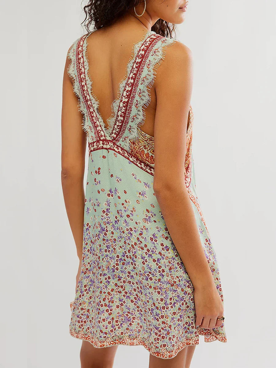 Mint - A woman wearing a sage green bohemian mini slip dress featuring a mixed ditsy floral and rust-colored paisley print, detailed with delicate eyelash lace trim along the V-neckline.