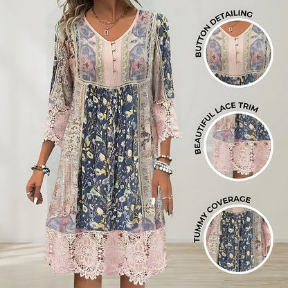 A woman wearing a bohemian-style mixed floral and paisley print shift dress with pink crochet lace trim on the 3/4 sleeves and hem, featuring a V-neckline with buttons, set against a scenic green hill and lake background.