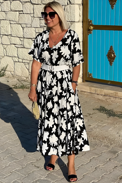 White - A woman wearing a black and white botanical leaf print maxi dress with a V-neckline and short sleeves, walking outdoors on a sunny day.