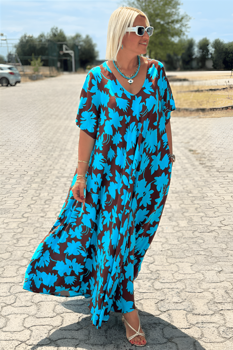 Blue - A woman wearing a black and white botanical leaf print maxi dress with a V-neckline and short sleeves, walking outdoors on a sunny day.
