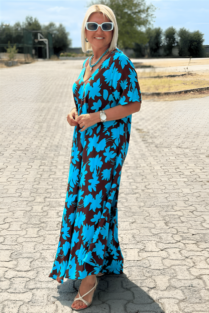 Blue - A woman wearing a black and white botanical leaf print maxi dress with a V-neckline and short sleeves, walking outdoors on a sunny day.