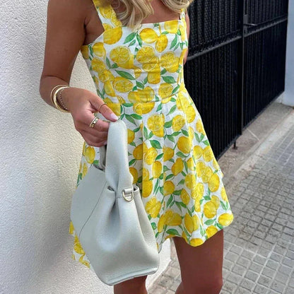 Yellow - Woman wearing a white mini dress with an all-over yellow lemon and green leaf print, featuring tie shoulder straps and a square neckline.