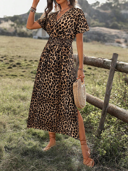 A woman wearing a leopard print maxi dress with a smocked waist, flutter sleeves, and a side slit, holding a woven straw bag in an outdoor setting.