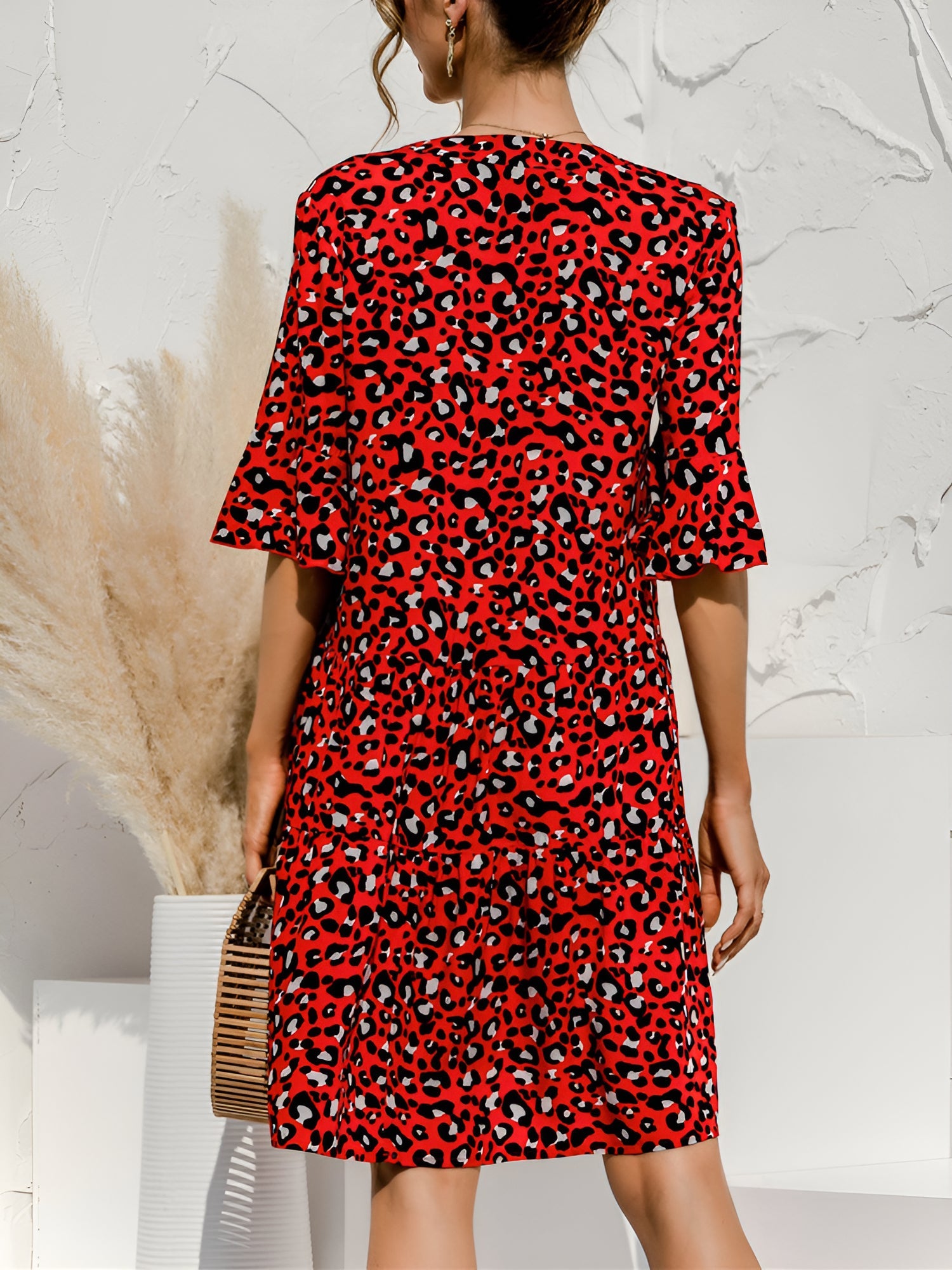 Red - Woman wearing a lightweight leopard print mini dress with flutter sleeves, a tie neckline, and a tiered skirt.
