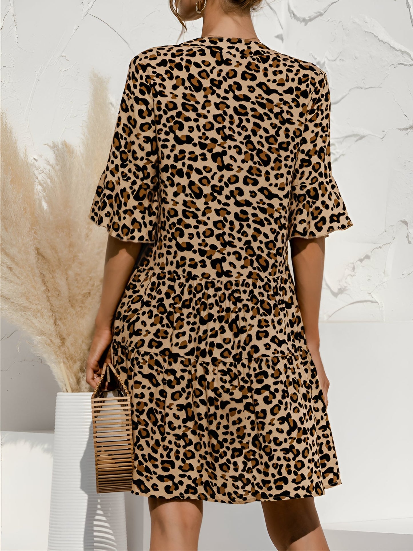 Leopard - Woman wearing a lightweight leopard print mini dress with flutter sleeves, a tie neckline, and a tiered skirt.