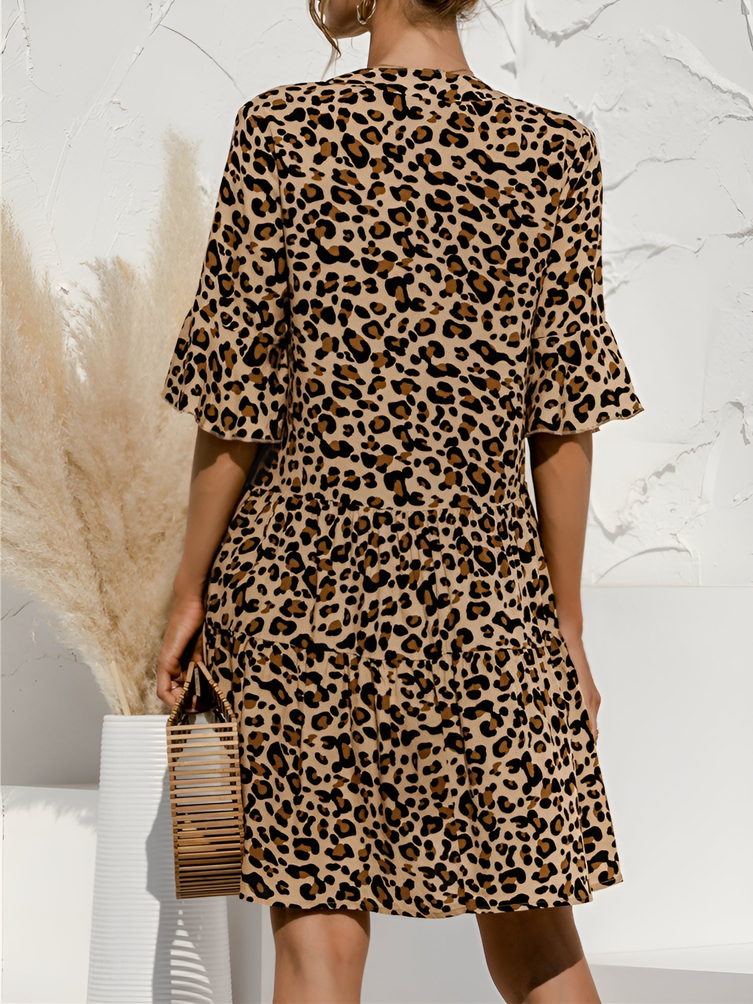 Leopard - Woman wearing a lightweight leopard print mini dress with flutter sleeves, a tie neckline, and a tiered skirt.