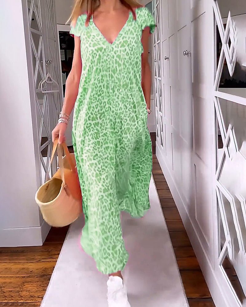 Green - A woman walks down a hallway wearing a pink leopard print maxi dress with a V-neckline and cap sleeves, carrying a woven straw tote bag.