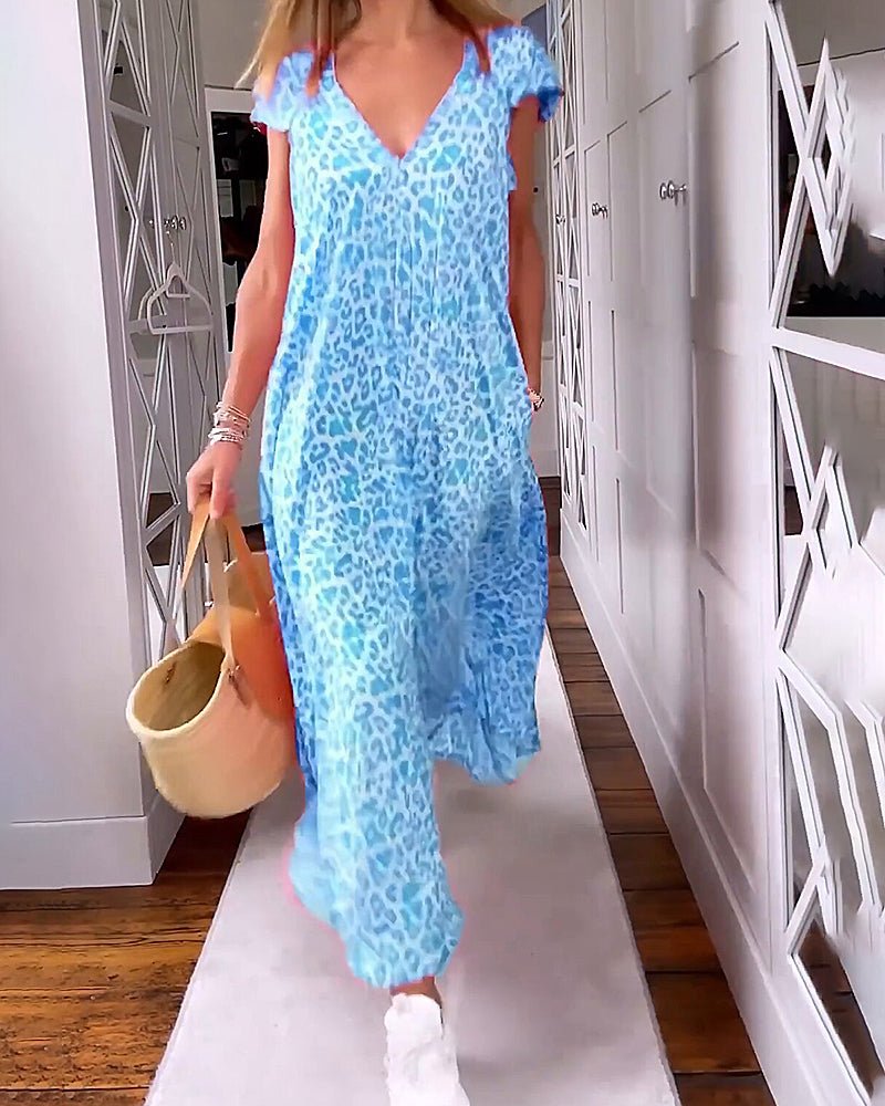 Blue - A woman walks down a hallway wearing a pink leopard print maxi dress with a V-neckline and cap sleeves, carrying a woven straw tote bag.