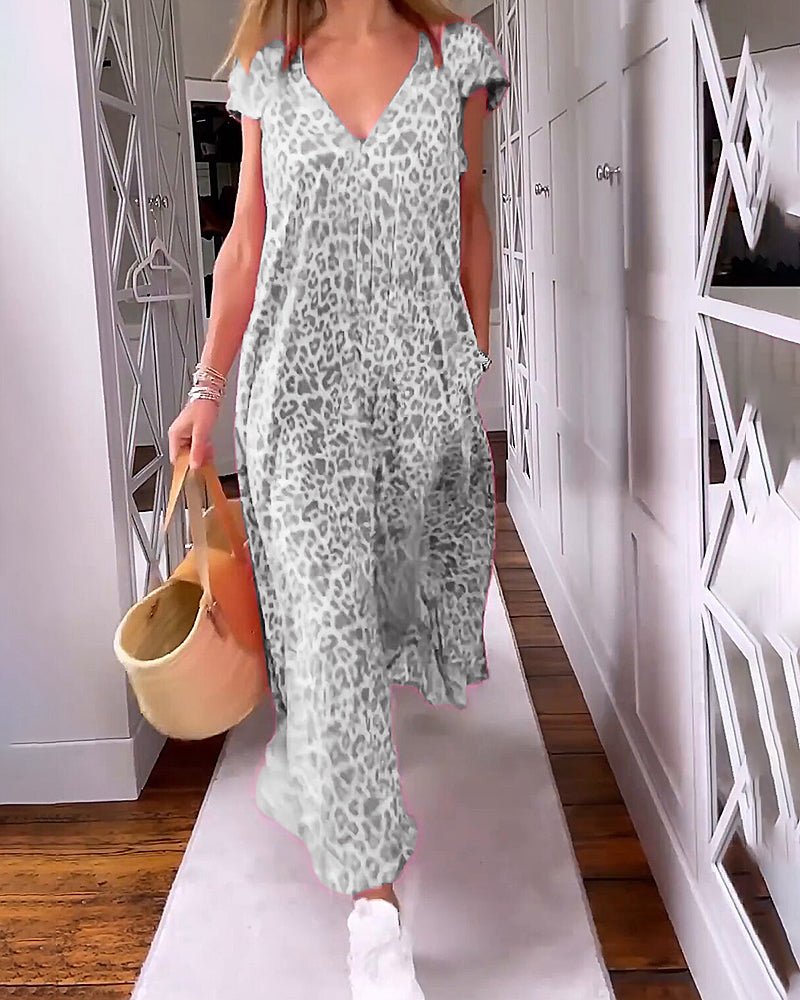 Grey - A woman walks down a hallway wearing a pink leopard print maxi dress with a V-neckline and cap sleeves, carrying a woven straw tote bag.