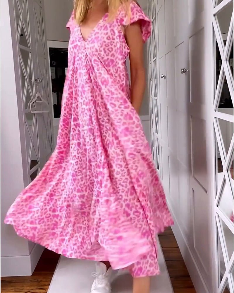 Red - A woman walks down a hallway wearing a pink leopard print maxi dress with a V-neckline and cap sleeves, carrying a woven straw tote bag.