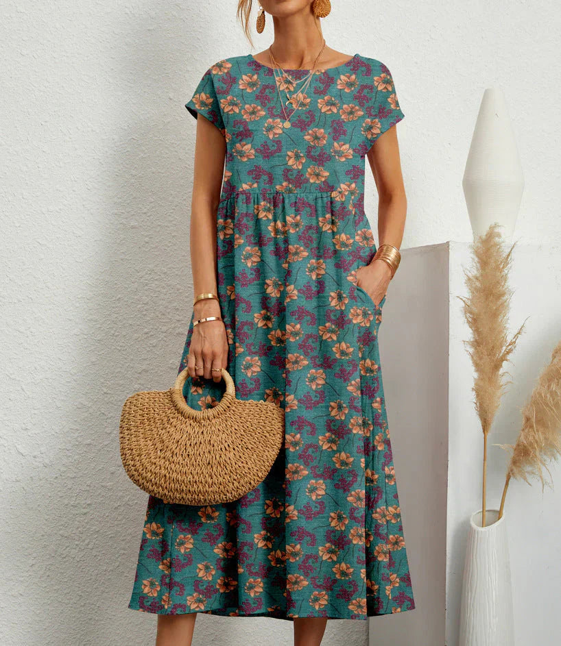 Teal Garden Bloom - A woman wearing a red and green kaleidoscope floral print linen-blend midi dress with cap sleeves and side pockets, holding a woven straw handbag.