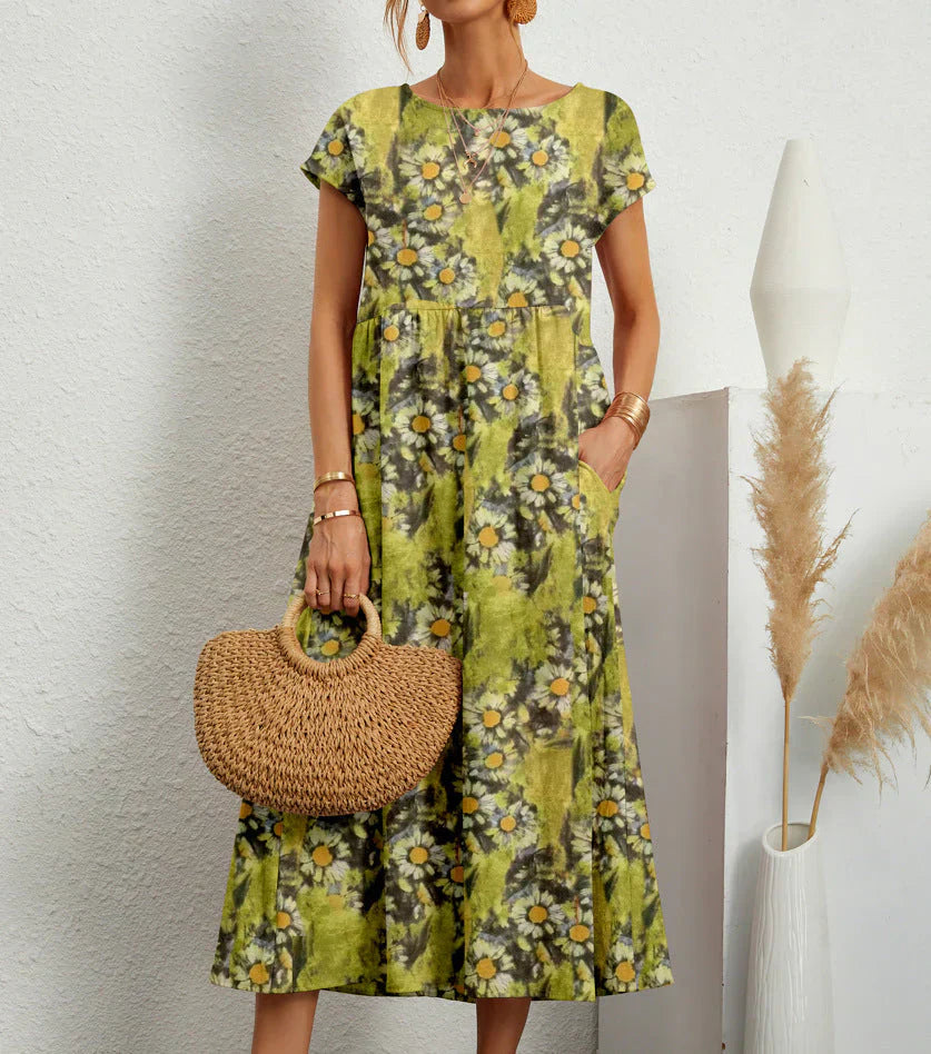 Daisy Forest - A woman wearing a red and green kaleidoscope floral print linen-blend midi dress with cap sleeves and side pockets, holding a woven straw handbag.