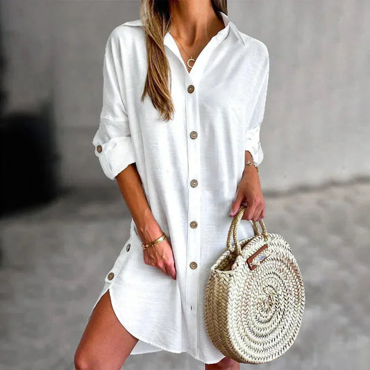 White linen button-front mini shirt dress featuring a collared neckline, rolled tab sleeves, and a curved hem with side button details.