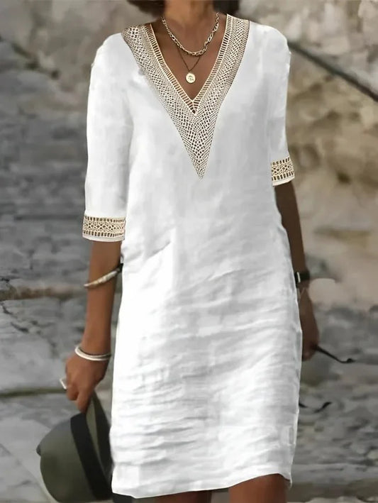 White - A woman wearing a white, knee-length shift dress made of textured linen-like fabric, featuring intricate beige crochet lace trim along the deep V-neckline and elbow-length sleeve cuffs.
