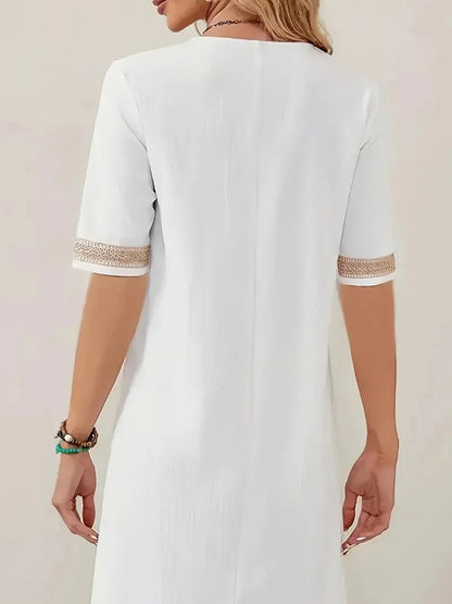 White - A woman wearing a white, knee-length shift dress made of textured linen-like fabric, featuring intricate beige crochet lace trim along the deep V-neckline and elbow-length sleeve cuffs.