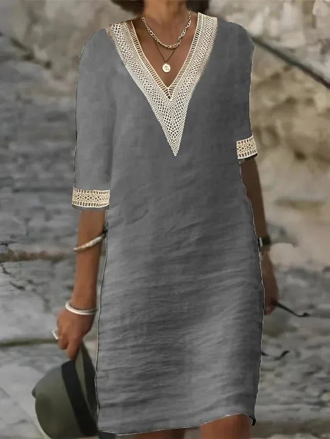 Gray - A woman wearing a white, knee-length shift dress made of textured linen-like fabric, featuring intricate beige crochet lace trim along the deep V-neckline and elbow-length sleeve cuffs.