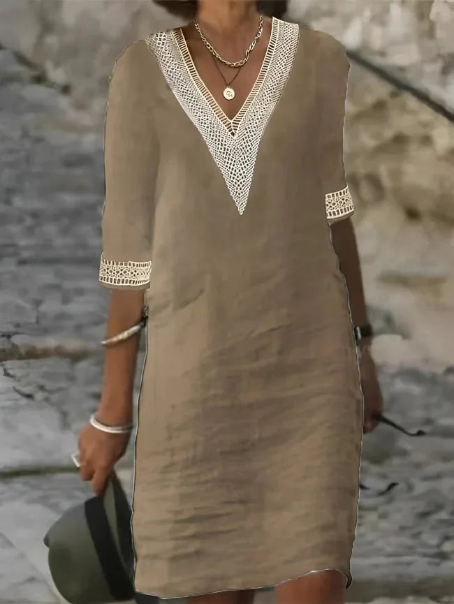 Beige - A woman wearing a white, knee-length shift dress made of textured linen-like fabric, featuring intricate beige crochet lace trim along the deep V-neckline and elbow-length sleeve cuffs.