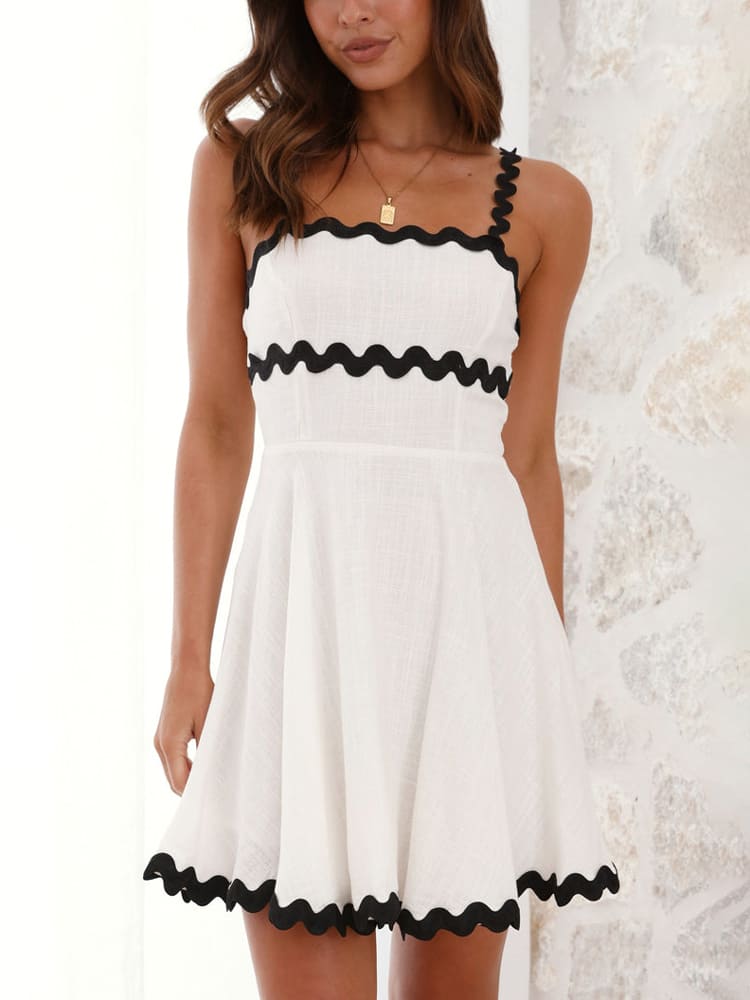 White - Close-up of a woman wearing a white sleeveless mini dress made of textured linen fabric, accented with contrast black scalloped rickrack trim on the bodice and flared hem.