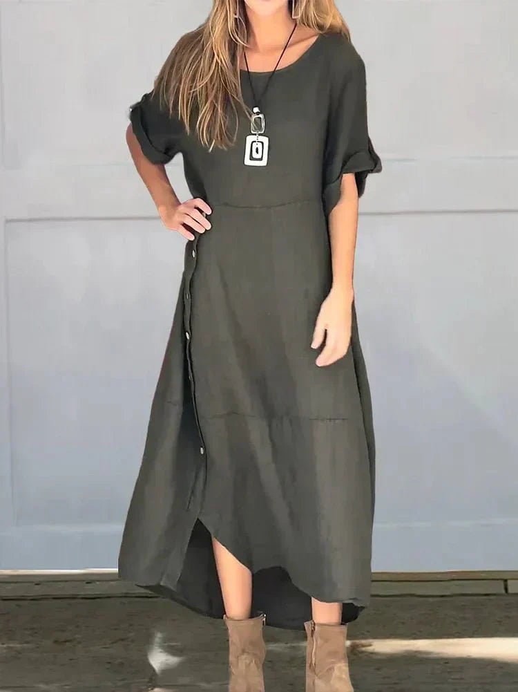 Dark Gray - A woman wearing a loose-fitting, taupe-colored textured linen maxi dress with short cuffed sleeves, a round neck, and a decorative side button placket down the front-right side.