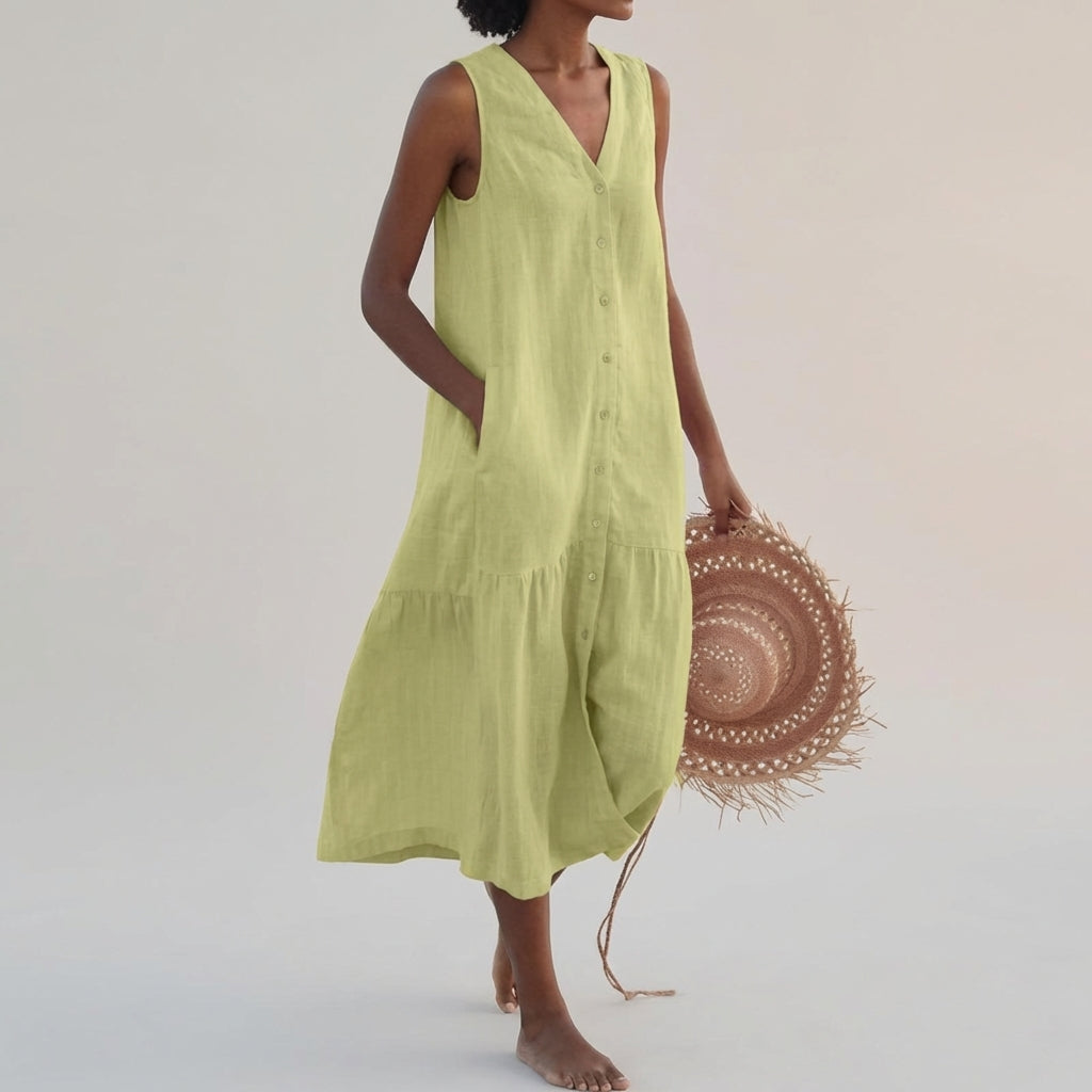 Green - A woman wearing a sleeveless white linen midi dress with a V-neck, button-down front, and tiered skirt, holding a wide-brimmed straw hat against a neutral background.