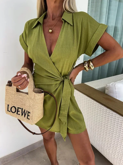 Green - Woman wearing a rust-colored linen-blend mini dress with a collar, deep V-neck, and tie waist, styled with sandals and a straw bag.