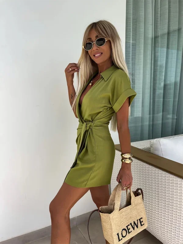 Green - Woman wearing a rust-colored linen-blend mini dress with a collar, deep V-neck, and tie waist, styled with sandals and a straw bag.