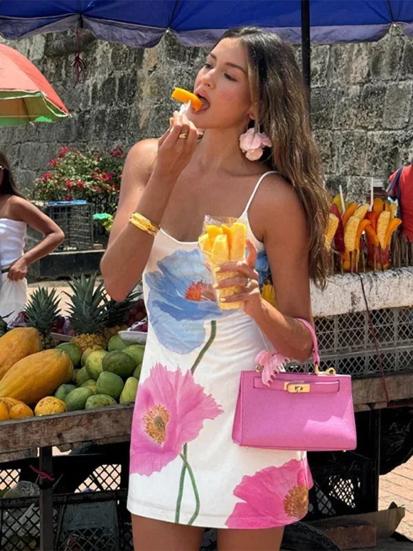White - Woman wearing a white slip mini dress featuring a large-scale pink and blue painted floral print, styled with delicate spaghetti straps and a straight neckline.